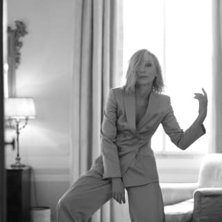 Cate Blanchette adopts an expressive pose, wearing a loose trouser suit and ruffled hair, photographed in black and white.