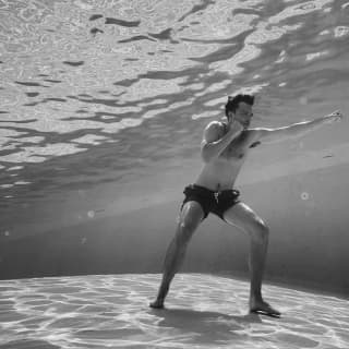 Nicholas Hoult, photographed by Greg Williams in black and white underwater as he stands on the pool bottom in a boxing pose.