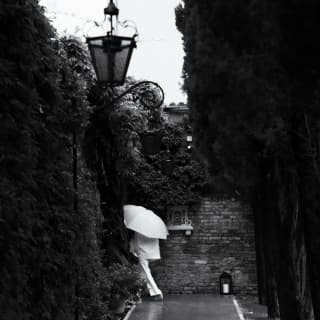 A guest dressed in white, carrying a white umbrella, disappears down a passageway in the hotel grounds, in black and white.