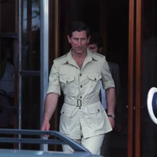 King Charles - then Prince - leaves the hotel in a pale beige safari suit with sleeves rolled up, watched by press and staff.