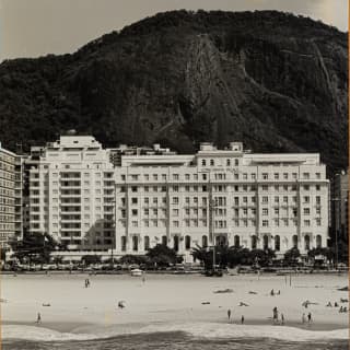 An historic black and white image of Copacabana Palace against the dramatic shape of Morro de São João, seen from the water.