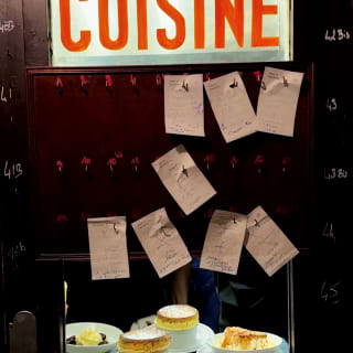 Soufflés sit in a dumb waiter pinned with order tickets and with an illuminated sign saying 'Cuisine', taken by Sam Youkilis.