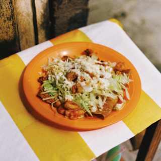 An orange plate of Enchiladas del Portal, comprising a tortilla with beans and vibrant fresh ingredients, seen from above.