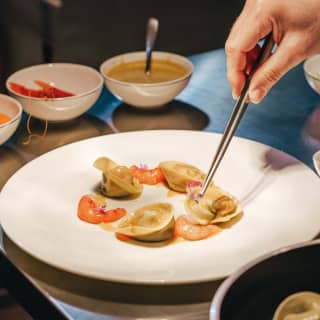 A fine dish of seafood pasta is assembled on a simple white plate on a shiny steel kitchen worktop