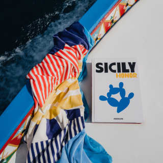 A copy of Sicily Honour rests on the deck of a boat with a pretty, hand-painted side, next to a red, blue and yellow towel.