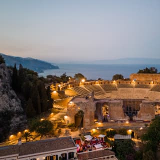 Golden lights dotted around the Teatro Antico di Taormina create a magical arena in the dusk gloom, seen from above.