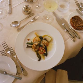 Looking down on a plate of king prawns, greens and buttery sauce at dinner on the Amaryllis, with wine, candles and cutlery.