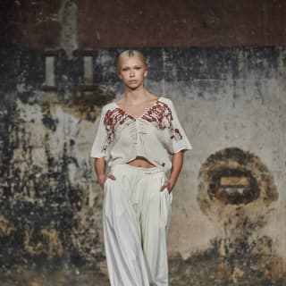 A model wears white, wide-legged Mercedes pants and cropped top with red embroidery and detailing, by Collectiva Concepción.