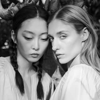 In black and white, two models pose in Yolanda tops, with split crewnecks and "Charro" braiding detail, by Collectiva Concepción.