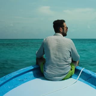 Maroma Executive chef, Daniel Camacho sits on the prow of a blue and white boat in Yucatán's sapphire sea, seen from behind.