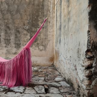 A sculptural hammock with sisal manes, based on a Mayan design, hangs in a stone courtyard, created by Fernando Laposse.
