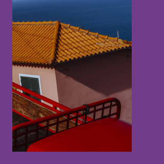 Artistic geometric image of a terracotta-roofed house with soft pink walls and ocean backdrop, seen over red railings.