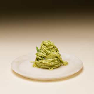 A perfect twirled mound of trenette pasta in a fresh, vibrant pesto sauce, served on a simple white plate, seen in close-up.