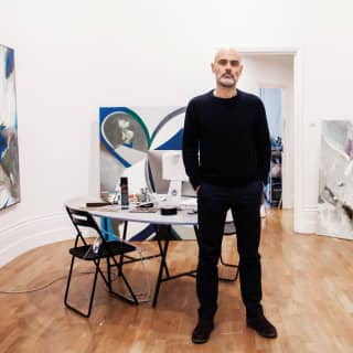 An artist stands among a collection of his modern abstract paintings