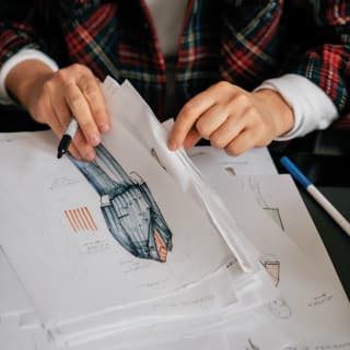 Close-up of two hands holding a pen and flicking through handrawn garment images