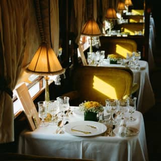 Gold light brushes the green velvet Etoile du Nord dining chairs, in a high-angle view over a laid tables with glowing lamps.