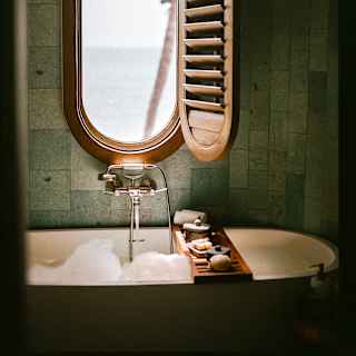 A shutter opens to reveal sea views through an oval window set in the wall above a bubbling bath with a cross-tub soap tray.