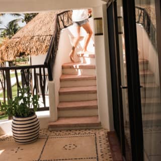 A guest, wearing shorts, runs up the stairs leading from a terrace to an upper level, seen from a shaded area by suite doors.