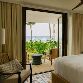 Open bedroom doors reveal a terrace, garden and immediate ocean views, seen over a large plump white bed in Villa Mariposa.