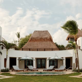 Beneath the palapa roof, the façade of Villa Maroma hugs the circular pool where four loungers recline beneath two parasols.
