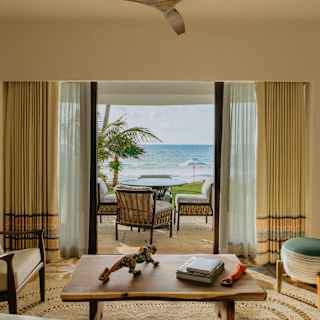 In Villa Maroma's living room, a stool and chair either side of a low table enjoy ocean views through open terrace doors.