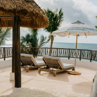 Two sun loungers next to a parasol face the ocean view on Villa Xuxú's terrace, viewed over the rippling private plunge pool.