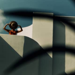Artistic image of a woman with a sunhat in front of her face as she stands on a terrace in Maroma's geometric roofscape.