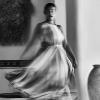A summer dress fans out in an artistic blur in this long-exposure black and white photograph of a woman as she turns around.