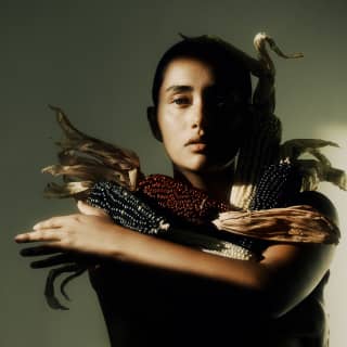 Artistic light and shade image of a female model holding Mexican heirloom red and black corn cobs against her chest.