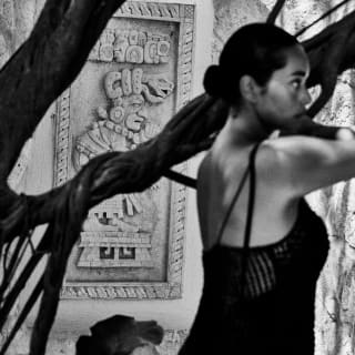 Jack Davison's chiaroscuro image of a woman standing next to a tree near the spa entrance, by a wall with a Mayan carving.