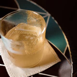 Close-up of Bambuco-branded ice cubes in a half-drunk cocktail in a tumbler set on a coaster on a tiled table top.