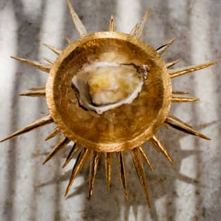 A raw oyster with pineapple and lemongrass is served in a theatrical gold dish with a halo of spikes at Woodend restaurant.
