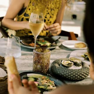 A female guest in a gold top enjoys oysters with white wine and salad, seen over the shoulder of her companion at Woodend.