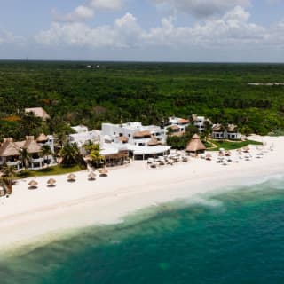 Aerial view of Maroma and its white pristine beach with thatched parasols, dividing the aquamarine sea from the lush land.