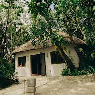A magical jungle location envelops a palapa with two front windows, housing La Casita Encantada kids club, seen from outside.