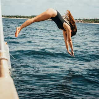 Action shot as a woman with long dark hair, wearing a black swimming costume, dives into the sea from a boat.