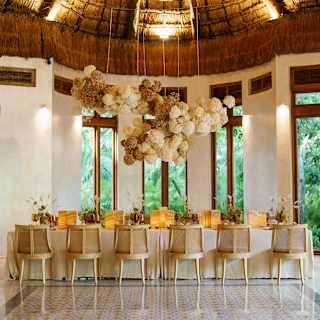 A dining table for twelve is ready for guests beneath decorative hanging pompoms and the high thatched roof of Palapa Tolok.