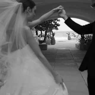 Black and white image of a bride and groom, in soft-focus foreground, as they dance on a terrace that leads to the open sea.