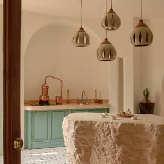 Pottery pendant lights hang over the Apothecary's central flat-topped rock table, with peppermint green cupboards behind.