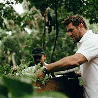 Woodend Chef Curtis Stone, in whites, and Adolfo Murillo in a black cap, pick greens in Maroma’s garden, seen at a low-angle.