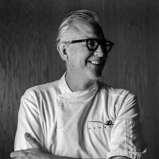 Chef Guillermo González Beristáin, in chef whites and dark-rimmed glasses, crosses his arms and looks to his left, smiling.