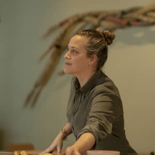 Chef Pía León, hair tied in a bun and wearing a khaki shirt with sleeves rolled up, reaches for a bowl in Mauka Restaurant.
