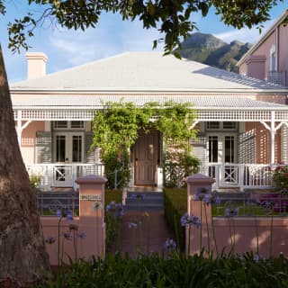 View of the quaint, double-fronted Honeysuckle Cottage with pink garden wall and trellis-like awnings, climbing with vines.