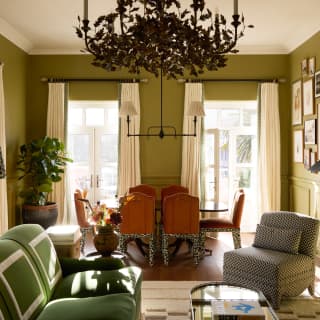 A chandelier hangs in Strelitzia's eclectic living space with a green sofa and dining table with red and animal-print chairs.