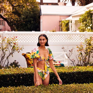 A smiling woman in a two-piece floral swimsuit standing in the garden