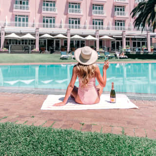 Lady in pink swim suit holding a glass of rosé champagne beside an outdoor pool
