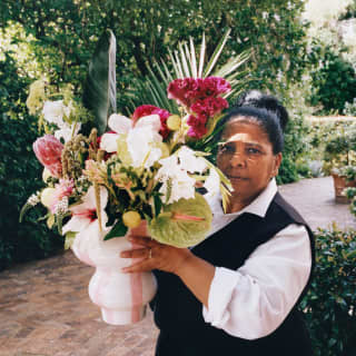 A staff member carries a white vase packed with white and pink flowers such as hibiscus and protea, and exotic leaf textures.