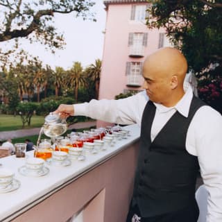 Rows of teacups and glass pots with flavoured brews line up on a terrace wall from where a staff member serves afternoon tea.