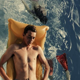 Hombre flotando en un colchón inflable naranja en una piscina