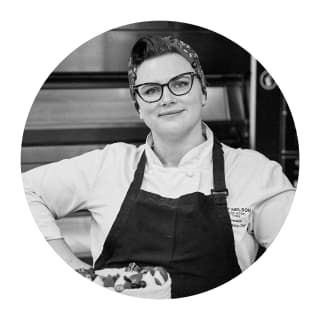 Porthole portrait in black and white of Head Pastry Chef, Vicky Gurovich, in a black apron, wearing glasses and hair bandana.